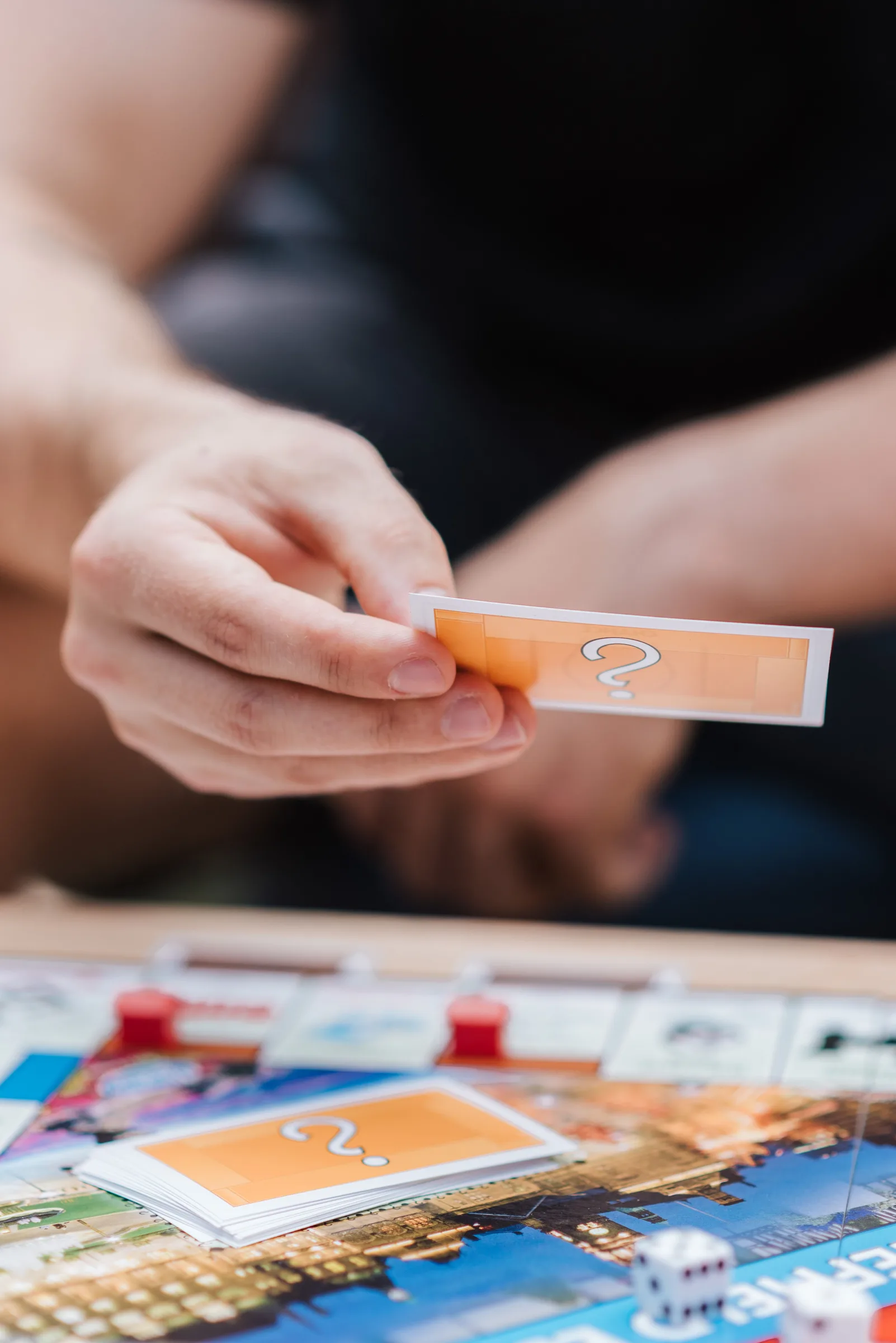 A person holds a game card above a board covered with small plastic houses and dice.